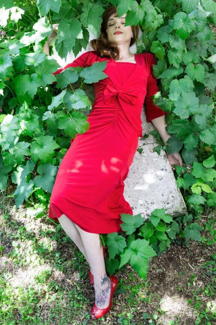 A woman lying on a stone while wearing a red tango dress