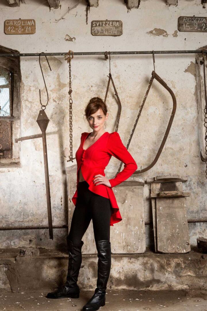 A woman in a V Argentine Tango Dress and black boots posing in an old building.