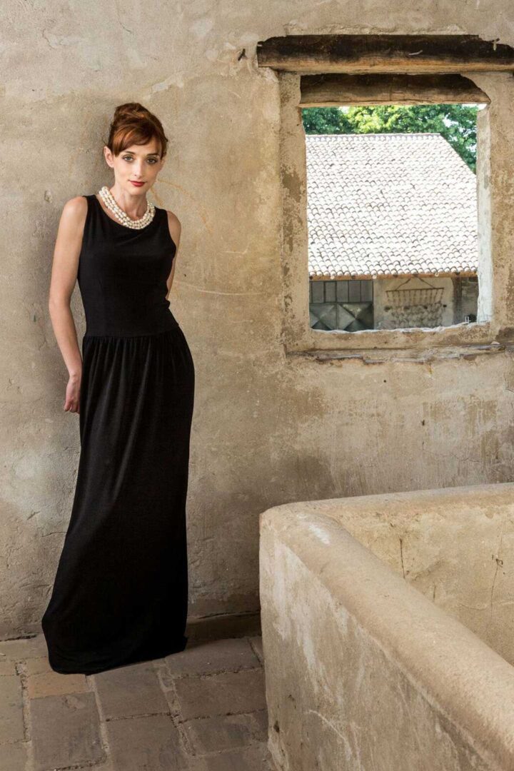 A woman in a black dress standing next to an old stone wall.