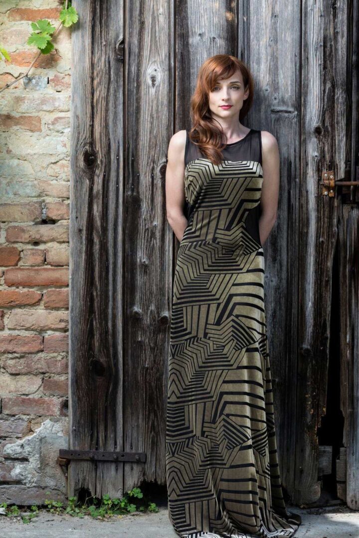 A woman in a Juana evening gown standing in front of a wooden door.