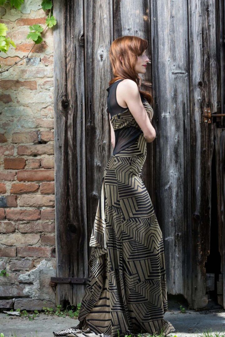 A woman in the Juana evening gown is standing in front of a wooden door.
