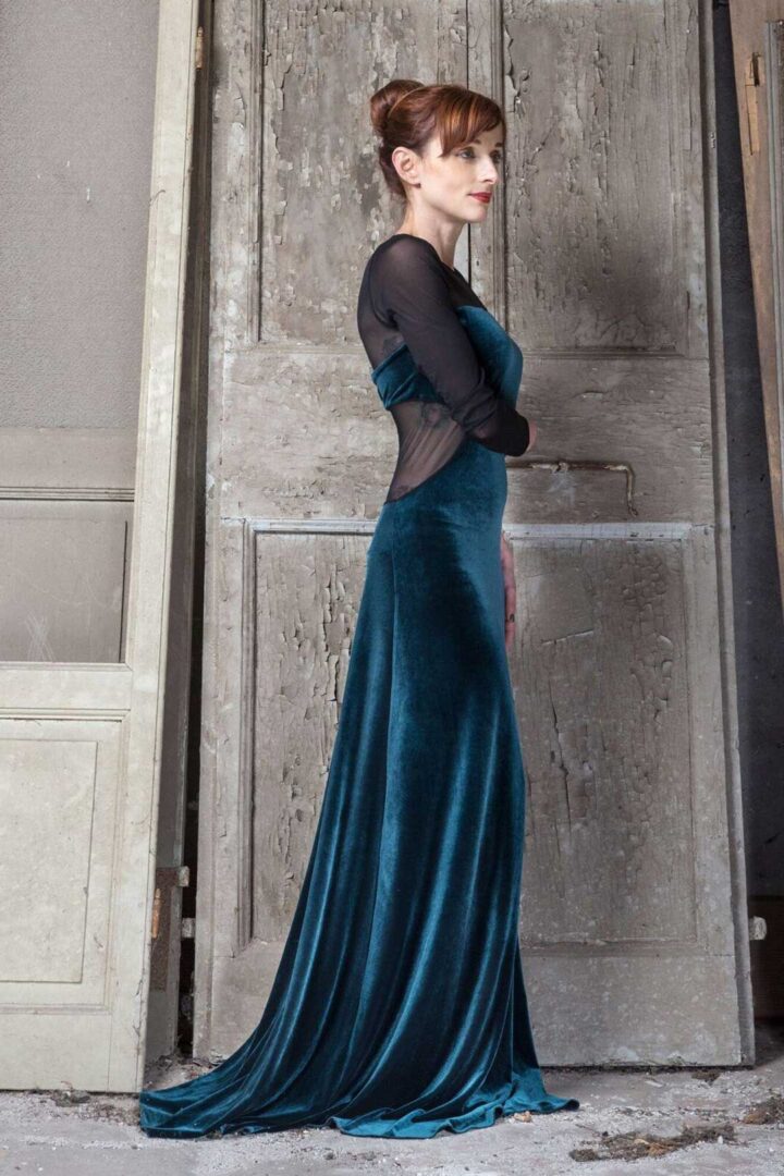 A woman in a teal velvet dress posing in front of an old door.