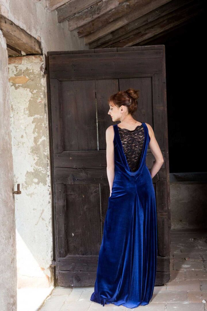 A woman in a Juana evening gown is standing in front of a wooden door.