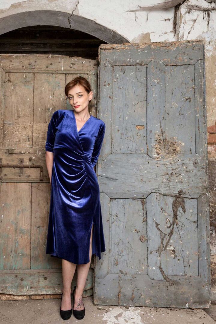 A woman in a blue velvet dress posing in front of an old door.