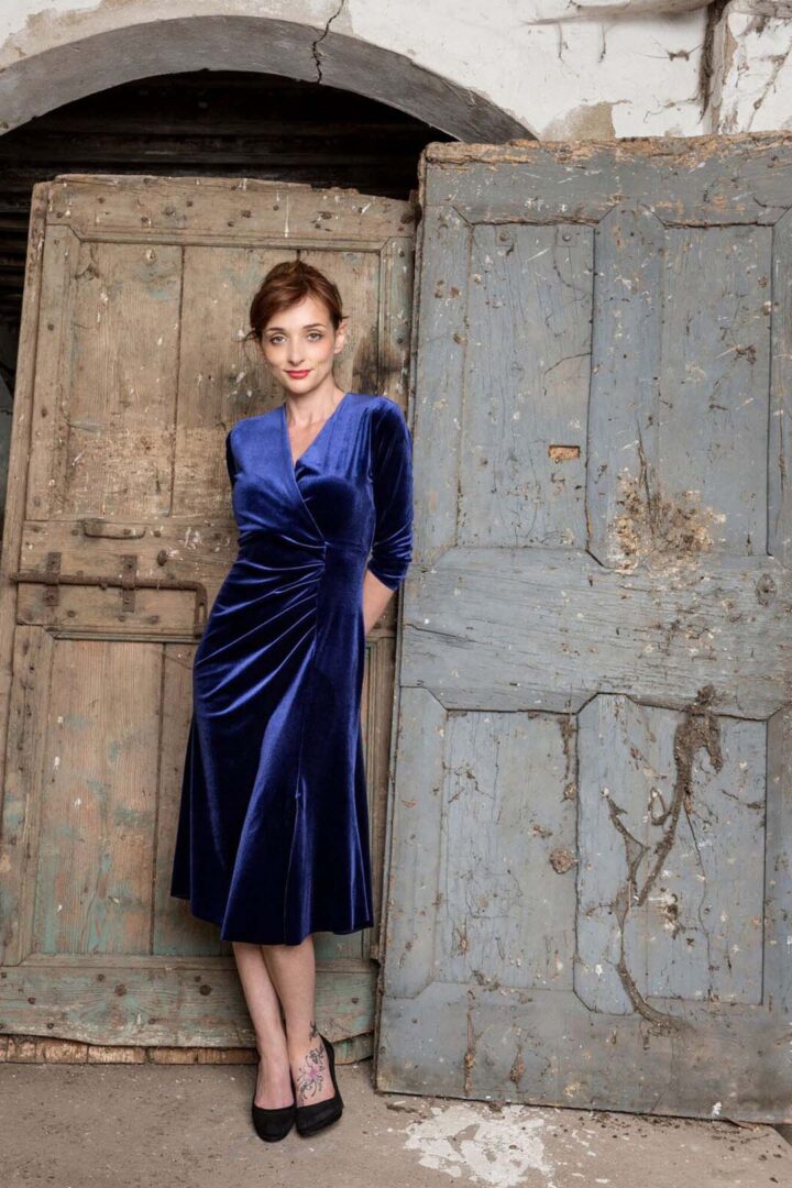 A woman in a blue velvet dress standing next to an old wooden door.
