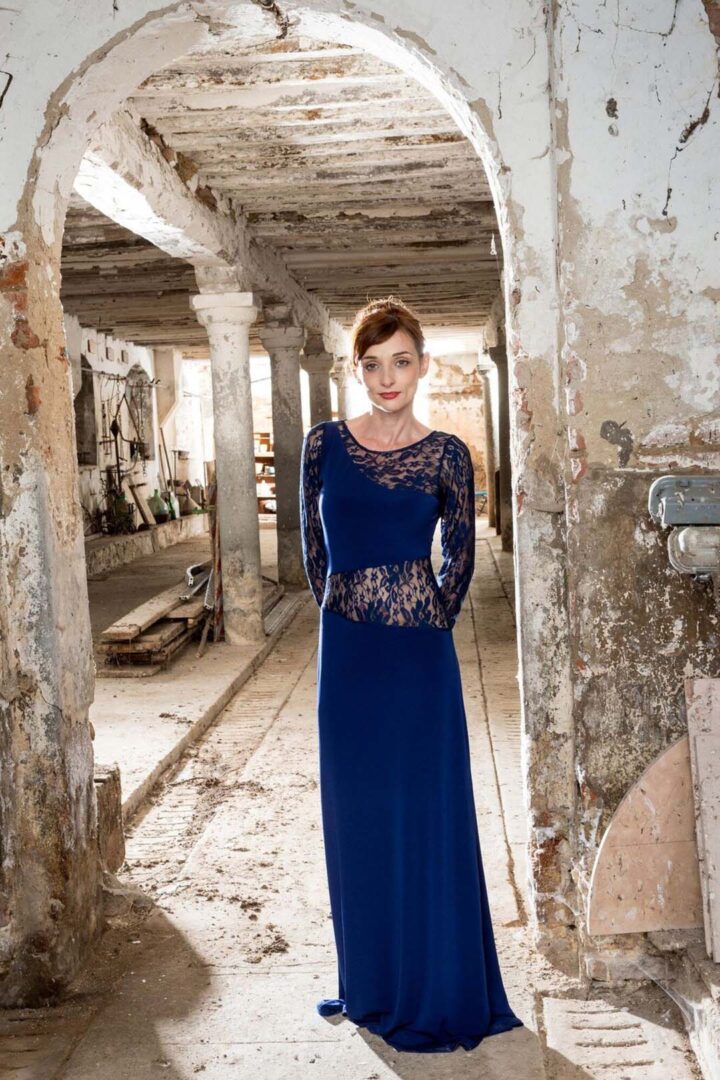 A woman in a blue dress standing in an abandoned building.