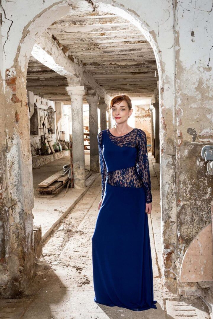 A woman in a blue dress standing in an abandoned building.