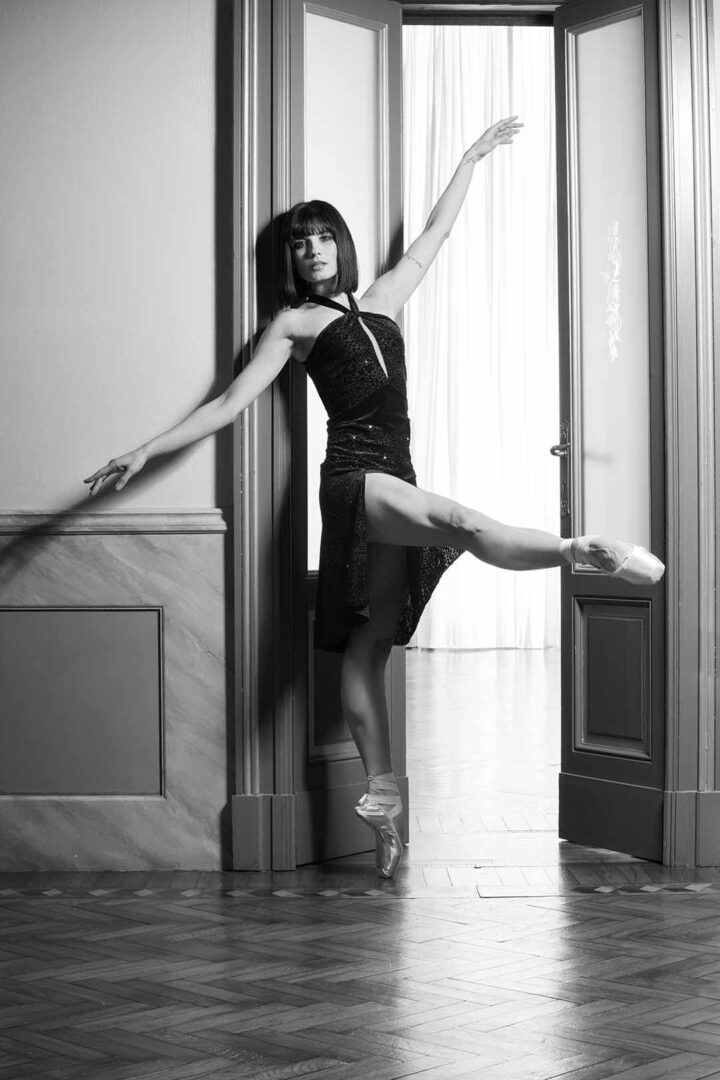 A black and white photo of a ballerina posing in a doorway.