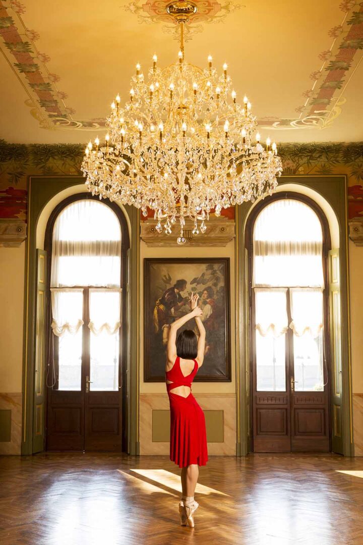A woman in a red dress is dancing in front of a chandelier.