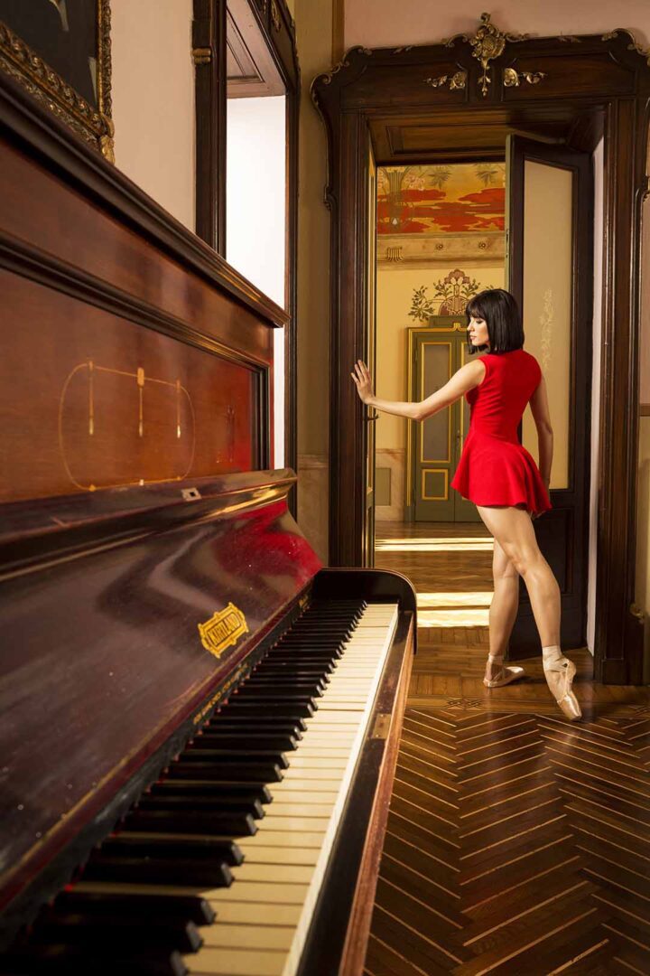 A woman in a red dress standing next to a piano.