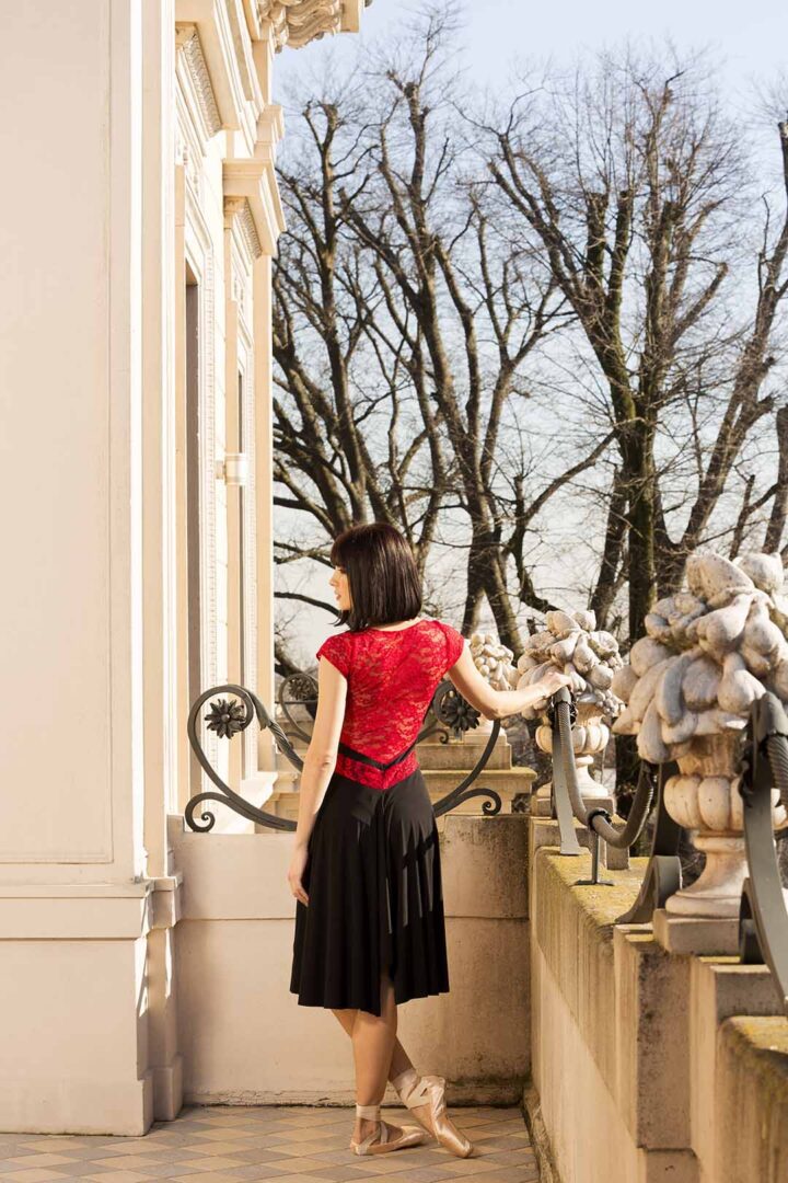 A woman in a red top and black skirt standing on a balcony.