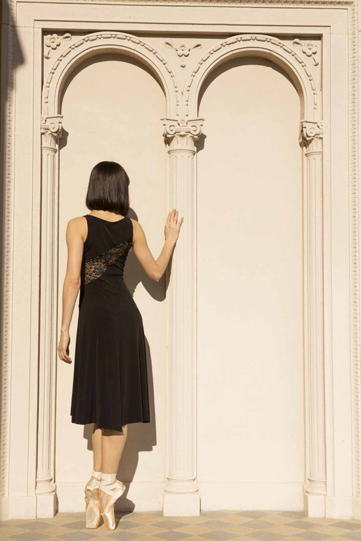 A woman in a black dress leaning against a wall.