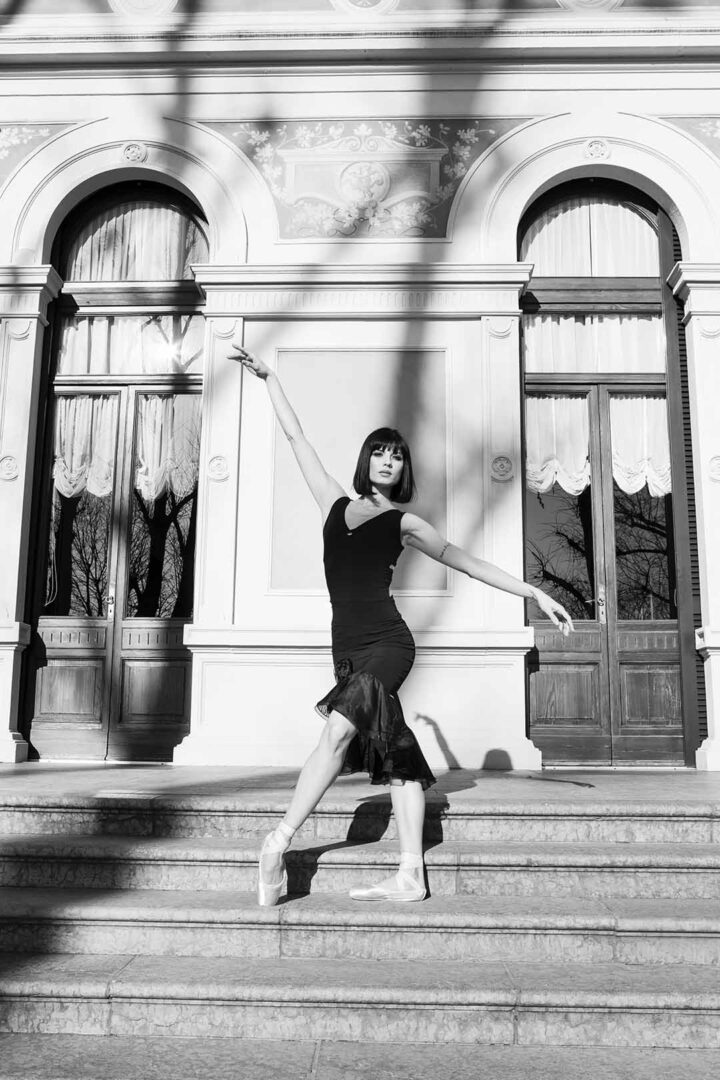 A black and white photo of a ballerina posing in front of an old building.