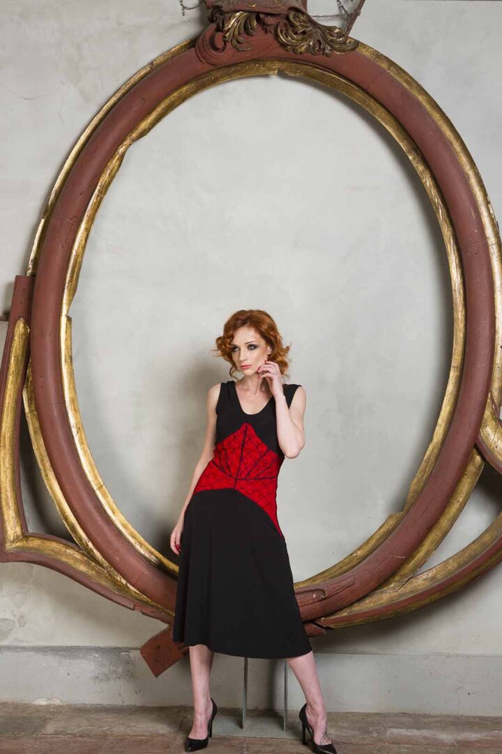 A woman in a black dress posing in front of an ornate frame.