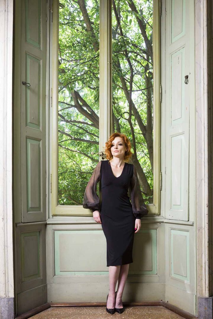 A woman in a black dress standing in front of a window.
