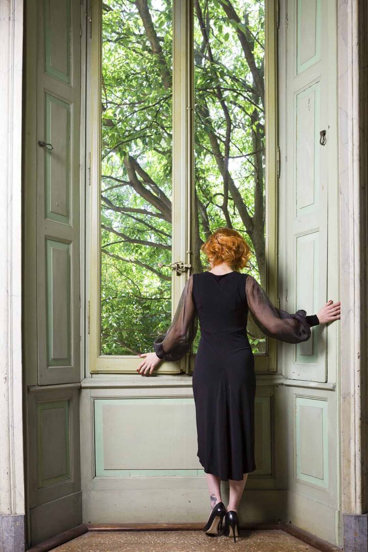A woman in a black dress looking out a window.