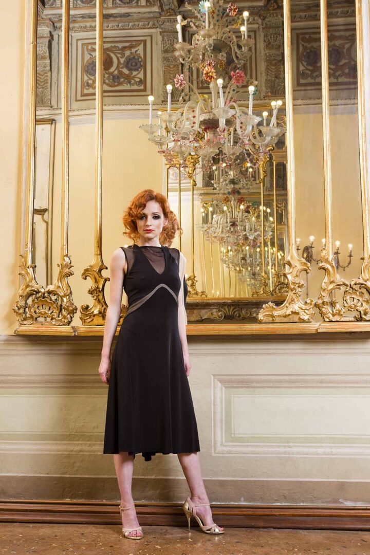 A woman in a black dress posing in front of a mirror.