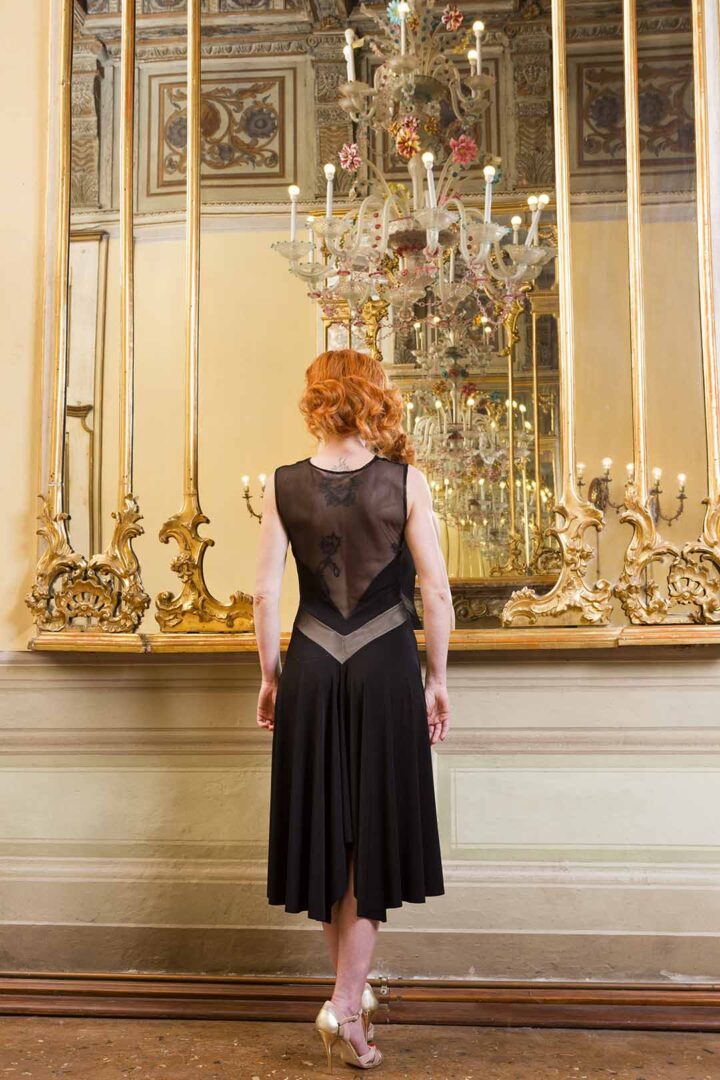 A woman in a black dress standing in front of a mirror.