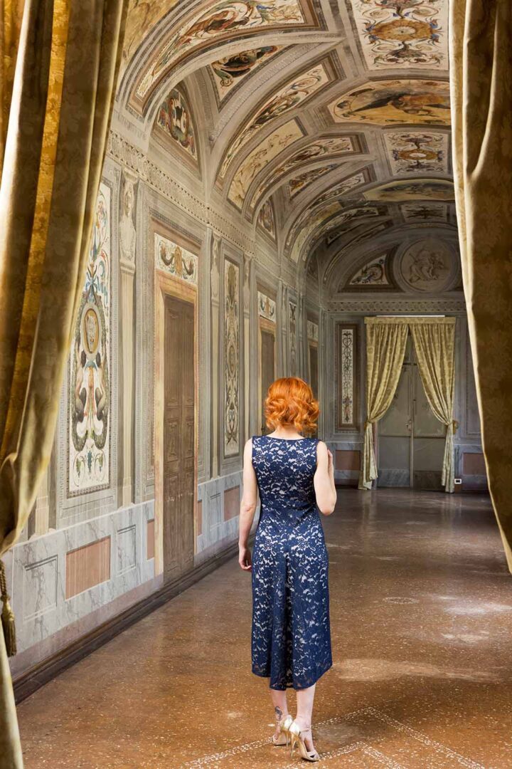 A woman in a red dress walks through an ornate hallway.