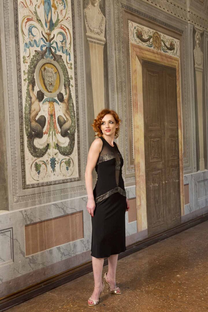 A woman in a black dress standing in an ornate room.