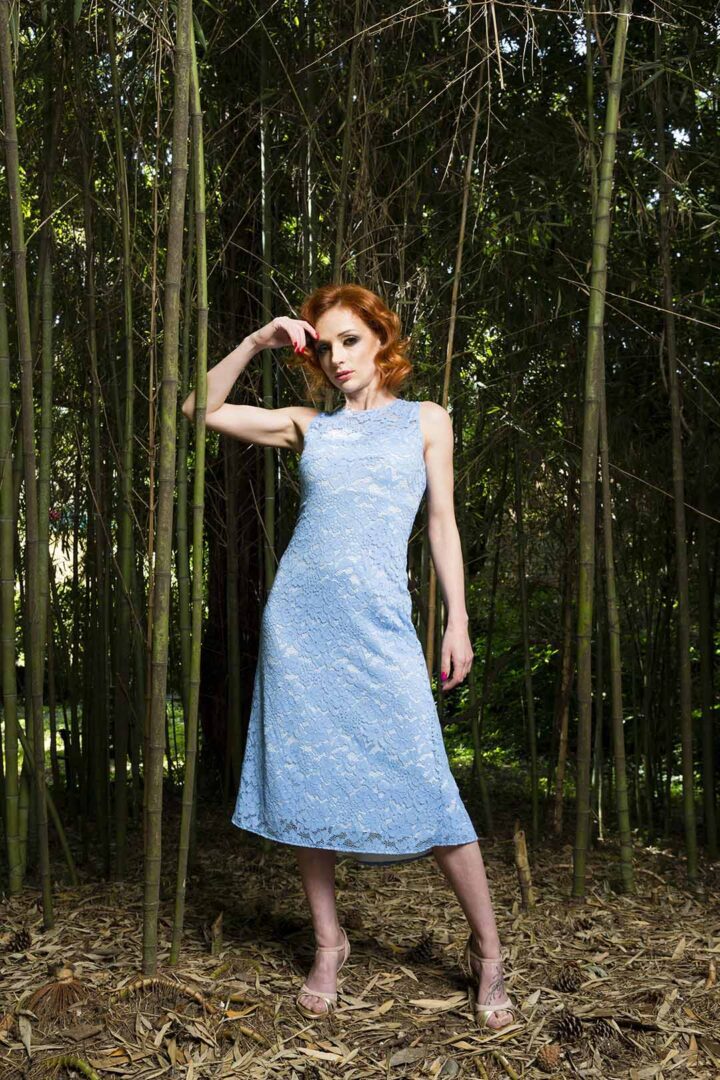 A woman in a blue dress posing in a wooded area.