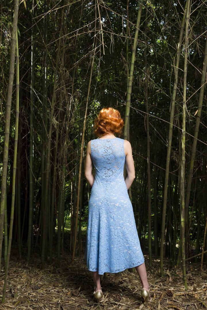 A woman in a blue dress standing in a wooded area.