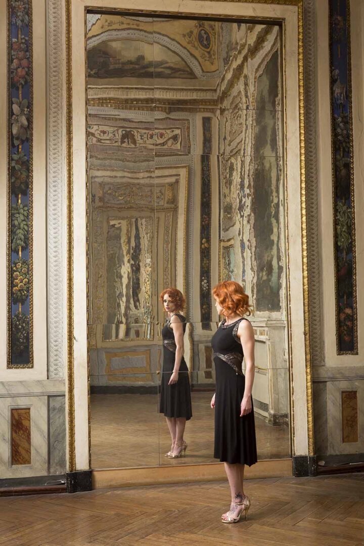 A woman standing in front of a mirror in an ornate room.