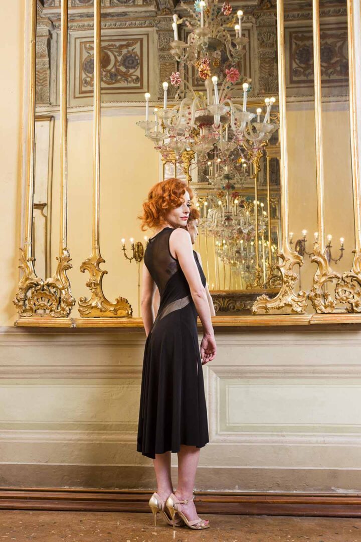A woman in a black dress standing in front of a mirror.