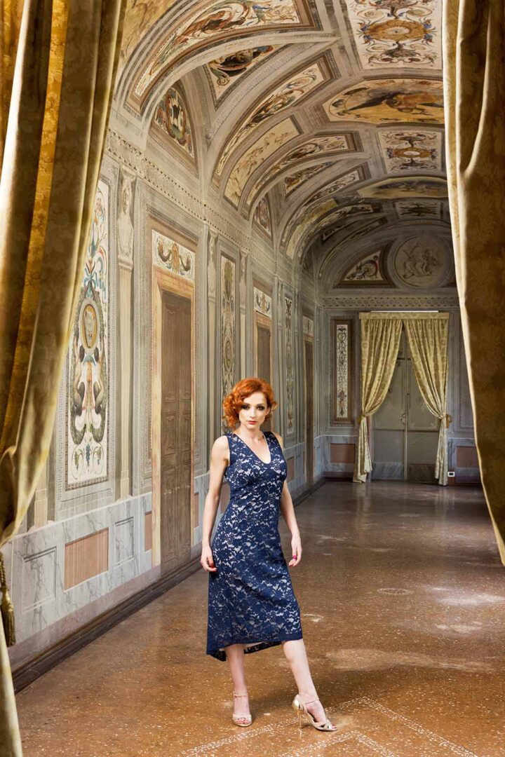 A woman in a blue dress standing in an ornate hallway.